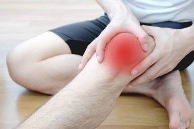 Genç adam dizinde ağrıyla oturuyor ve elini dizinde kötü hissediyor. Sağlık hizmetleri kavramları.