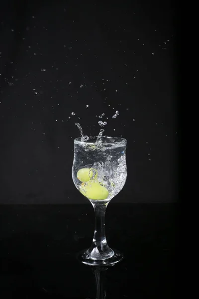 Water splash out of glass on a black background. With green grapes.