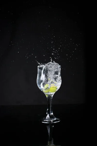水在黑色的背景上从玻璃杯中喷出 用绿色葡萄 — 图库照片