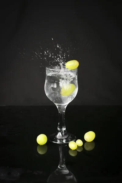 Water splash out of glass on a black background. With green grapes.