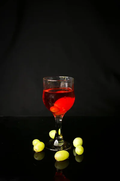 水在黑色的背景上从玻璃杯中喷出 用绿色葡萄 — 图库照片