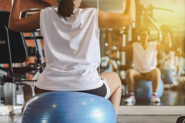 Kadın halterlerle spor yapıyor jimnastik topunda oturuyor..