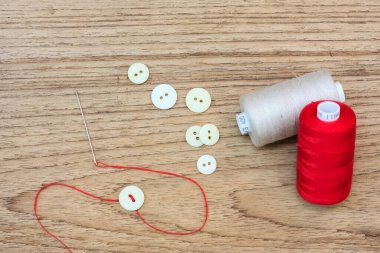 Renkli iplik bobinleri, düğmeler ve tahta zemin üzerinde metin alanı olan iğne.