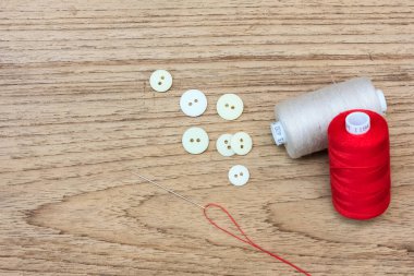 Renkli iplik bobinleri, düğmeler ve tahta zemin üzerinde metin alanı olan iğne.