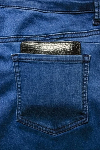 Black leather wallet in back blue jeans pocket denim background texture.