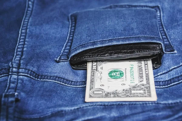 Black leather wallet with money in back blue jeans pocket denim background texture.