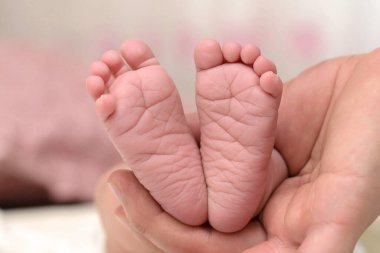 Yeni doğmuş bir bebeğin ayakları yakın plan, baba bebeğin küçük ayaklarını eliyle tutar ve gösterir.