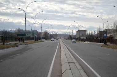 Şehirdeki otoyol dağların arka planına ve bulutlu gökyüzüne doğru gidiyor, yolda arabalar gidiyor.