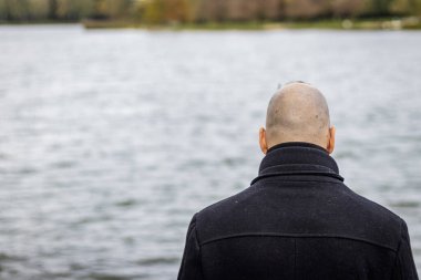 Kötü havada bir adam gölün kıyısında duruyor.