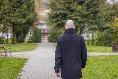 Yerel parkta damlayan yağmurda bir adam yürüyor.