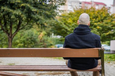 Yerel parktaki damlayan yağmurda bir adam kırık bir bankta oturuyor.