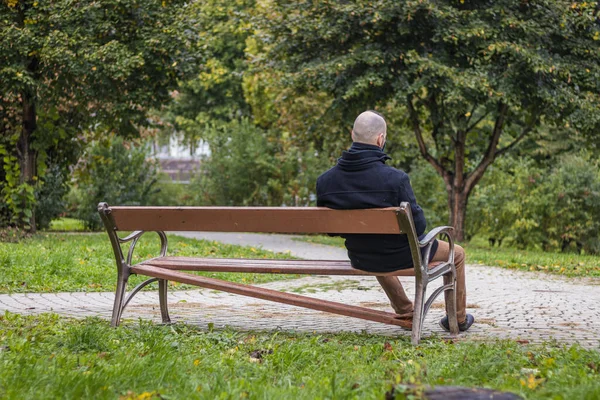 Yerel parktaki damlayan yağmurda bir adam kırık bir bankta oturuyor.