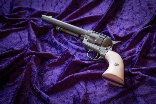 Old wild west revolver with white wood grips over purple velvet