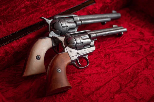 Old wild west revolvers with brown and white wood grips over red velvet