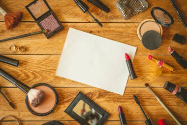 Etrafında makyaj malzemeleri olan ahşap bir masaya not yazmak için boş bir sayfa..