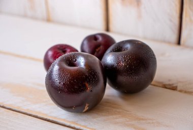 Beyaz ahşap bir duvarda ve masada koyu olgun erikler..