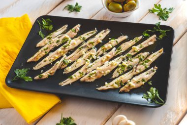 Koyu dikdörtgen bir tabakta ançüez turşusu beyaz tahta bir masada diğer atıştırmalıklarla birlikte. Tipik İspanyol yemekleri barda yenir..