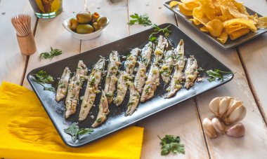Koyu dikdörtgen bir tabakta ançüez turşusu beyaz tahta bir masada diğer atıştırmalıklarla birlikte. Tipik İspanyol yemekleri barda yenir..