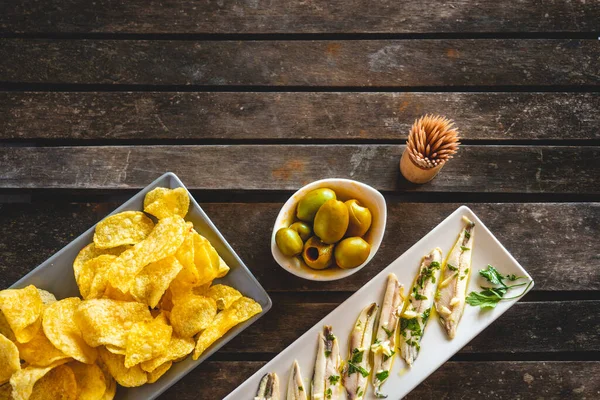 三道菜 马铃薯片 采摘的凤尾鱼和绿色橄榄在黑暗的木制桌子上与牙签 在酒吧里吃的典型西班牙小吃 — 图库照片
