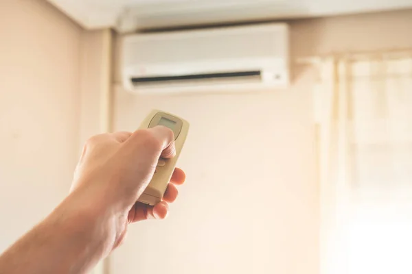 Hand with air conditioner remote control changing the home temperature. Photo with selective focus.