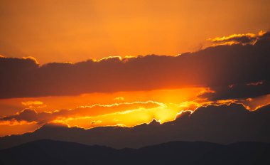 Turuncu gökyüzü, arka planda bulutlar ve gün batımında batan güneş.. 