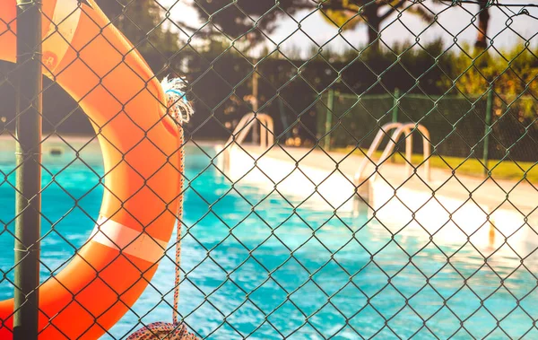 View of a salt water pool from the fence with a orange life float on a sunny summer day.