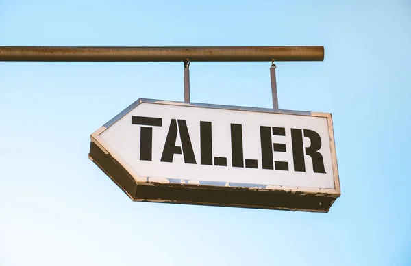 Sign hanging in the street indicating that there is a mechanical workshop, with the spanish word taller, on a sunny day.