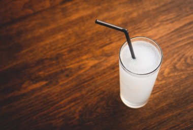 Kahverengi ahşap bir masanın üzerinde siyah plastik kamışla yakın plan buzlu limon camı. Seçici odaklı fotoğraf.