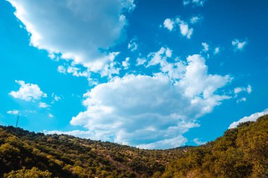 Güneşli bir günde, dağların üzerinde bulutlarla mavi gökyüzü ve yeşil orman..
