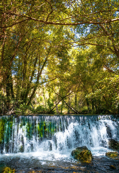 Natural waterfall called Cascada del Hervidero in Madrid, in the forest, with sunlight between vegetation and rocks. 