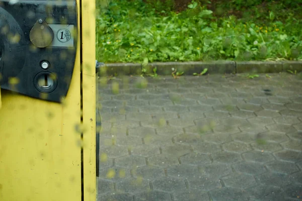 Yellow vacuum cleaner, in parking lot, with a Euro coin slot, photographed through rain window pane, depth of field, Germany.