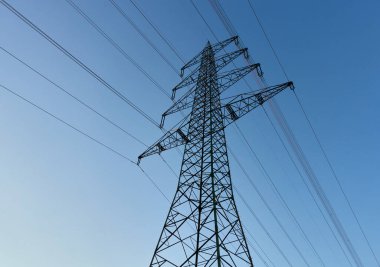 Büyük Elektrik pilonunun silueti aynı zamanda mavi gökyüzünde tepedeki pilon hattında, kablolar resim boyunca çapraz olarak çalışıyor. Almanya.