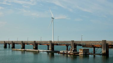 Uzun çelik ve ahşap iskele suyun üzerinde, büyük rüzgar türbini barajın üzerinde. Hollanda, Vrouwenpolder.