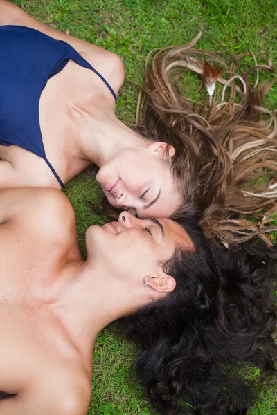 Hermosa pareja joven con el pelo largo están tumbados en la hierba. Vista desde el punto superior . — Foto de Stock