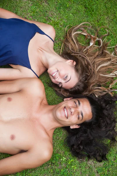 Hermosa pareja joven con el pelo largo están tumbados en la hierba. Vista desde el punto superior . — Foto de Stock