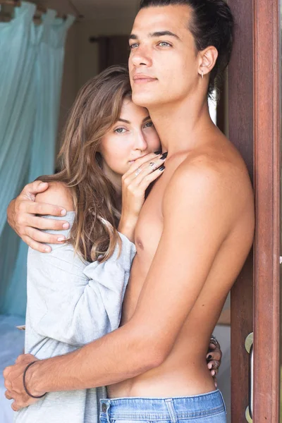 Genç çekici yakışıklı gülümseyen adam ve kadın kapıda sarılma. Kız bir hoodie giyinmiş. adam çıplak bir gövde ile