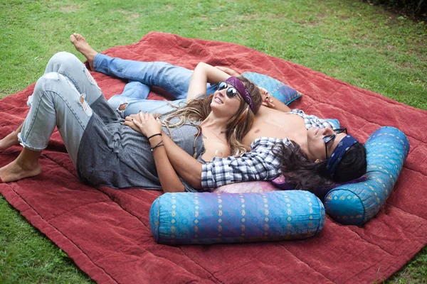 Joven atractivo sonriente hombre y mujer con el pelo largo y en gafas de sol están acostados en la alfombra con almohadas. Hippie y estilo gitano . — Foto de Stock