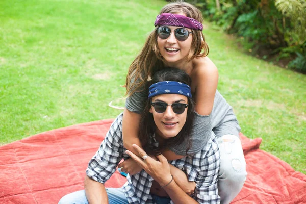 Young attractive smiling man and woman with long hair and in sunglasses are sitting on the carpet with pillows. Hippie and gypsy style. — Stock Photo, Image