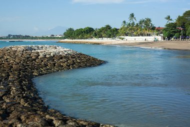 taş sahil, palmiye ağaçları ve mesafe bir yanardağ ile deniz manzarası. Bali