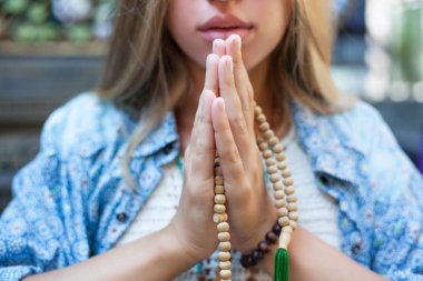 genç bir kadının yakın portresi. Elleri dua için göğsünün önünde katlanmış. Elinde boncuklar var. Meditasyon