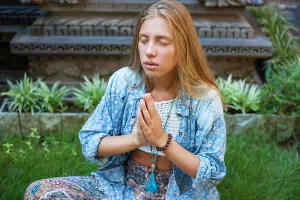 Piękna młoda kobieta siedzi na trawie w pozycji lotosu z zamkniętymi oczami i medytacją. — Zdjęcie stockowe