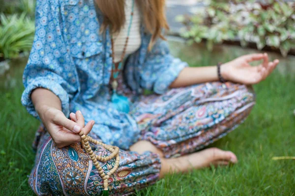 Retrato de braços femininos no joelho. A menina está sentada na posição de lótus e mantendo as contas de oração Yoga, meditação . — Fotografia de Stock