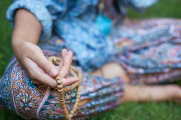 Retrato cercano de una mano femenina en su rodilla manteniendo cuentas de oración. La chica está sentada en la posición de loto. Yoga, meditación . — Foto de Stock