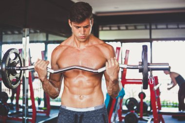 çekici seksi genç çıplak göğüslü adam egzersiz Asansör halter ayakta yapar. Gergin yüz ve vücut