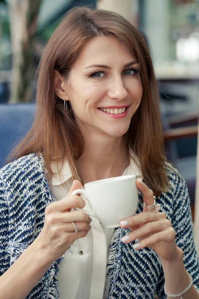 Retrato de atractiva morena sonriente joven mujer de negocios. La niña sostiene una taza blanca en sus manos y mira a la distancia — Foto de Stock