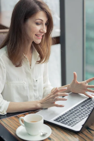 Atractiva joven mujer de negocios en una camisa ligera se sienta en una mesa con un ordenador portátil. Tiene emociones fuertes en la cara. Sus manos están tensas, los dedos separados. La computadora es lenta. Irritabilidad — Foto de Stock