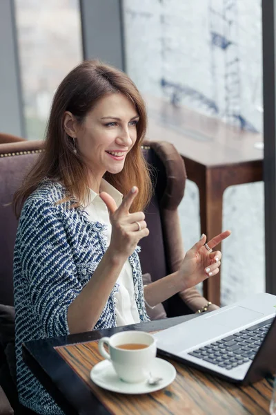 Attractive young business woman sits at a table with a laptop. Sly smile on her face. Eureka. Bingo. Index fingers in the form of a gun.