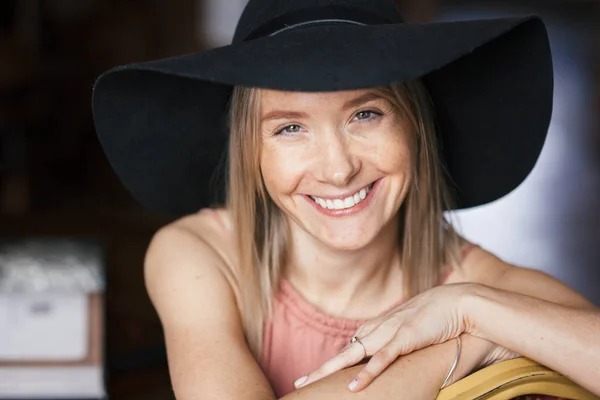 Cerrar retrato romántico cálido de una hermosa joven rubia sonriente feliz con pecas en vestido de color rosa ceniza y sombrero de fieltro negro. Chica sentada dentro — Foto de Stock