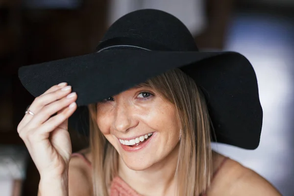 Cerrar retrato romántico cálido de una hermosa joven rubia sonriente feliz con pecas en vestido de color rosa ceniza y sombrero de fieltro negro. Chica sentada dentro — Foto de Stock