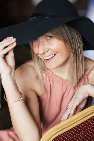 Kül gül renkli elbise ve siyah keçe şapka çiller ile güzel bir mutlu gülümseyen genç sarışın kadının yakın sıcak romantik portre. Evde oturan kız